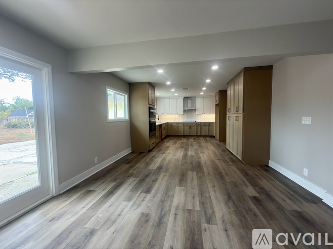 A spacious room with wooden flooring and a large window on the left side.