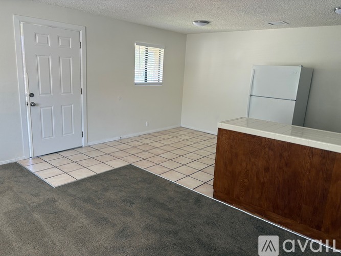 A room with a white door, a window with blinds, a wooden cabinet, and a tiled floor.