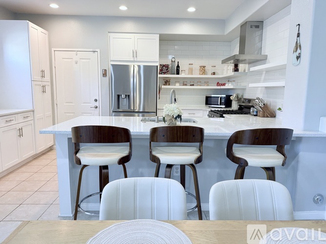 A kitchen with white cabinets and a white island with four chairs.