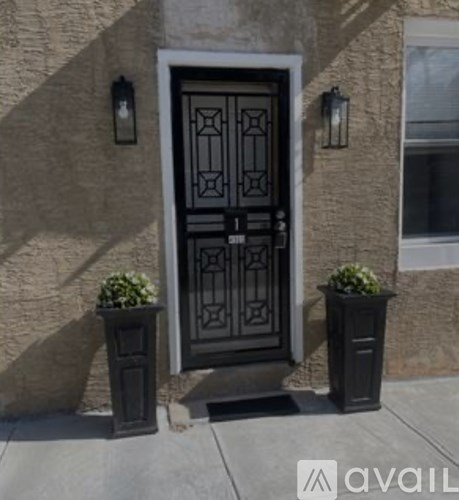 A black door with a glass window is flanked by two black planters.