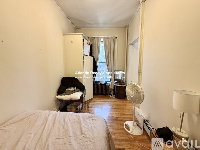 A bedroom with a bed, a fan, a chair, and a window with curtains.