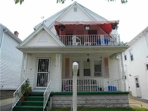 A white house with a red awning and a green staircase.