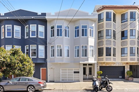 A grey car is parked in front of a grey and blue building.