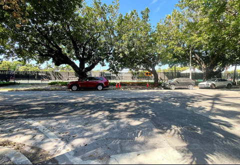 A red car is parked in a lot with trees.