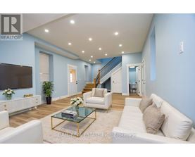 A living room with a white couch, a glass coffee table, and a staircase in the background.