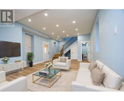 A living room with a white couch, a glass coffee table, and a staircase in the background.