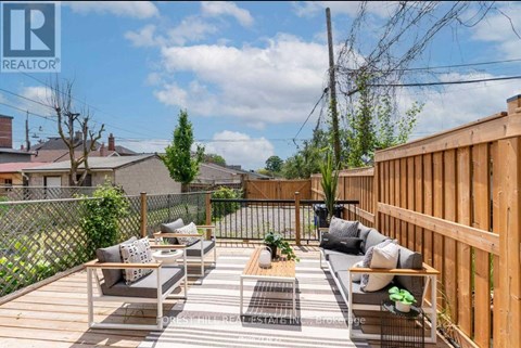 A wooden deck with a couch and a coffee table is surrounded by a fence.