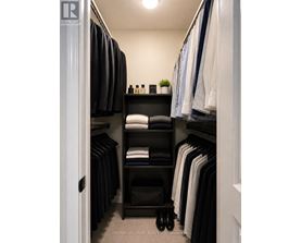 A well organized walk in closet with a shelf and clothes hanging.