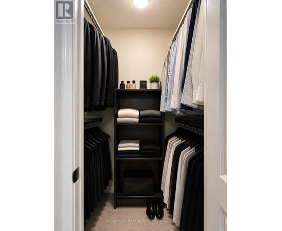 A well organized walk in closet with a shelf and clothes hanging.