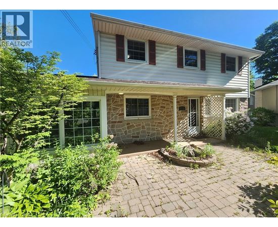 A house with a white siding and a stone pillar in the front yard.