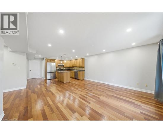 A large empty room with wooden floors and a kitchen area in the background.
