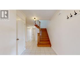 A white hallway with a wooden staircase and a white door.