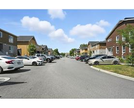 A row of cars parked on a street in front of apartment buildings.
