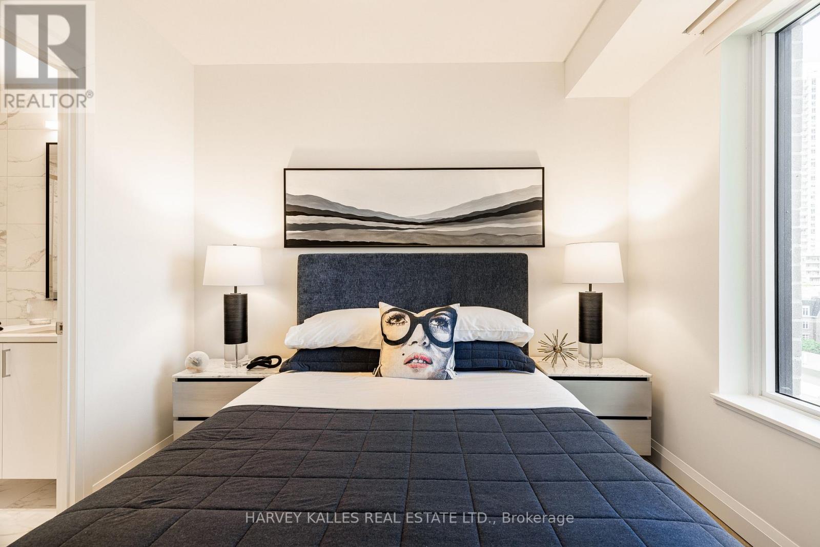 A bedroom with a large bed and a painting of a woman's face on the pillow.