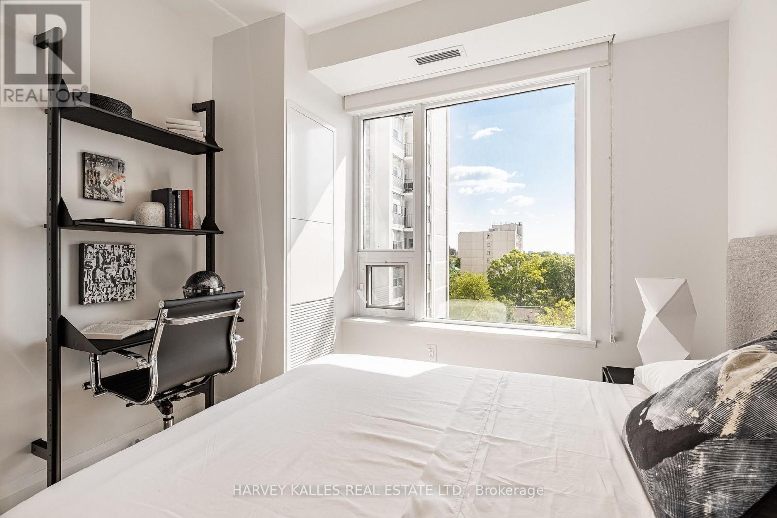 A bedroom with a large bed, a desk with a chair, and a window overlooking a cityscape.