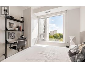 A bedroom with a large bed, a desk with a chair, and a window overlooking a cityscape.