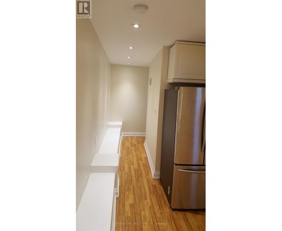 A stainless steel refrigerator in a kitchen with wooden floors and white walls.