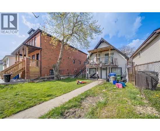 A realtor photo of a house with a red brick exterior and a white house with a black fence in the background.