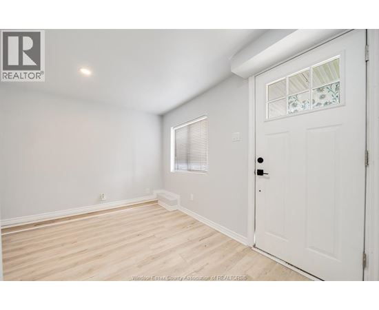 A white door is on the right side of a room with a window and a light on the wall.