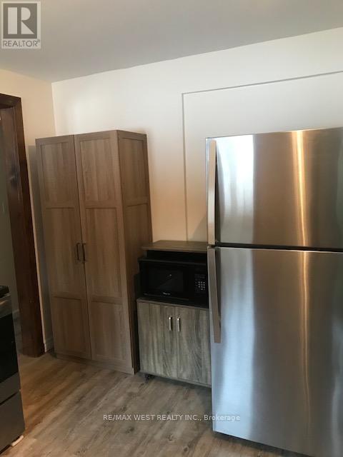 A stainless steel refrigerator stands next to a wooden cabinet and microwave in a kitchen.