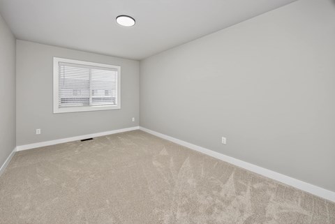 A room with a carpeted floor and a window with blinds.