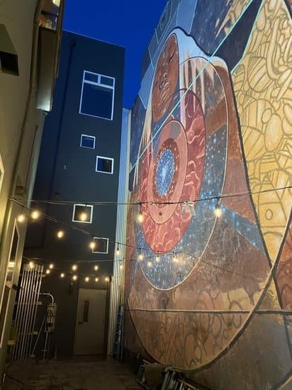A mural of a large hand holding a smaller hand is illuminated by string lights.