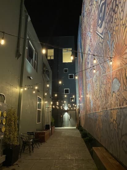 A narrow alleyway with string lights and a mural on the wall.
