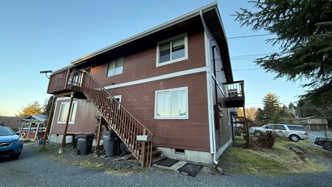 A brown house with a white stripe on the side and a balcony on the second floor.