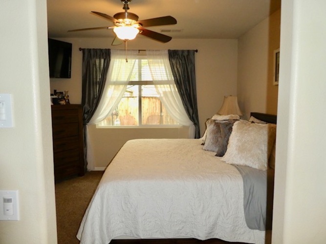A bedroom with a bed, a ceiling fan, and a window with curtains.