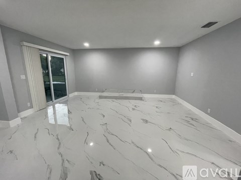 A spacious room with marble flooring and a sliding glass door.