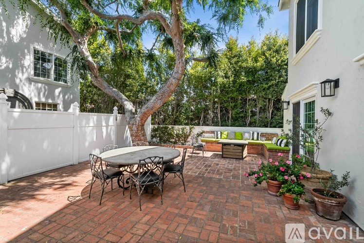 A patio with a table and chairs surrounded by a white fence and trees.