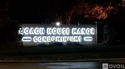A sign for Coach House Manor Condominiums is lit up at night.