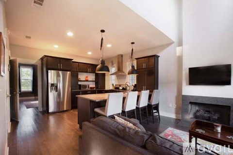 A modern kitchen with a refrigerator, a dining table with chairs, and a fireplace.