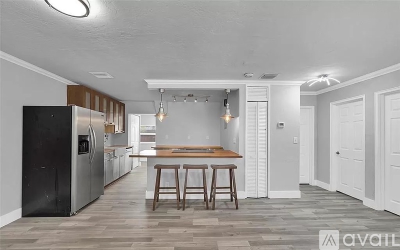 A kitchen with a black fridge, wooden bar stools, and a wooden table.