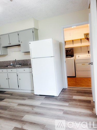 A white refrigerator in a kitchen with wooden flooring.