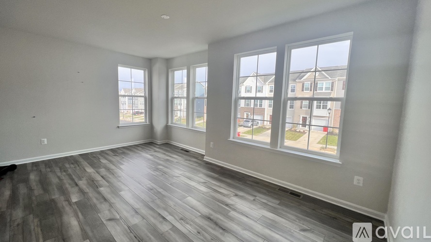A spacious room with grey flooring and large windows overlooking a residential area.