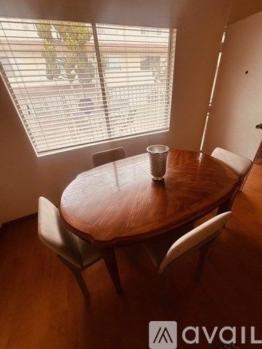 A wooden table with four chairs is in a room with a window showing a parking lot outside.