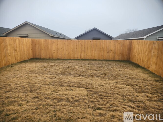 A backyard with a wooden fence and brown grass.