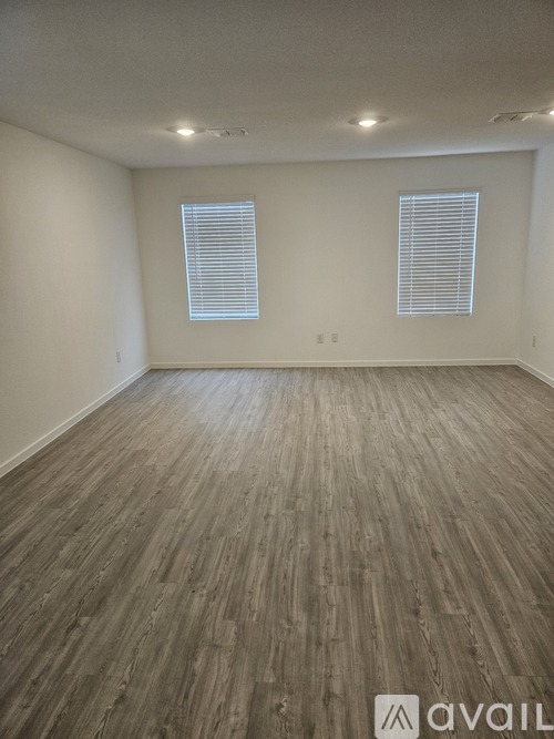 A room with wooden flooring and two windows.