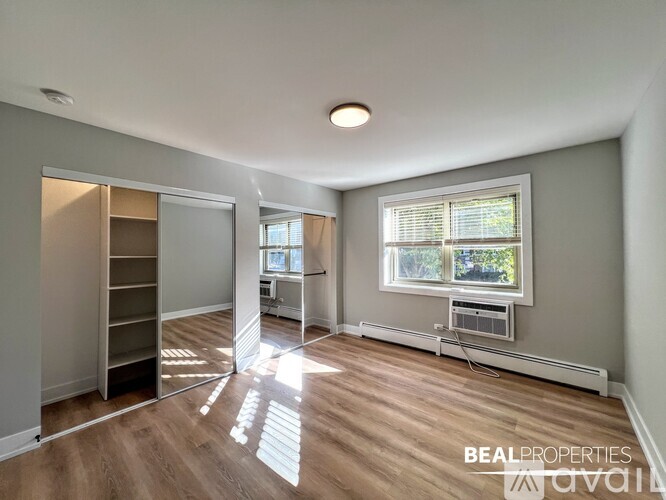 A spacious room with wooden flooring and a large window with blinds.