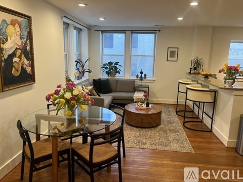 A living room with a glass table and chairs, a grey sofa, and a painting on the wall.