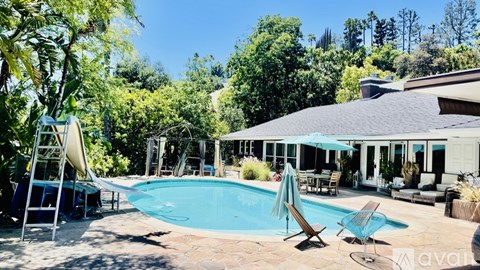 A pool with a sun lounger and a table in front of a house.