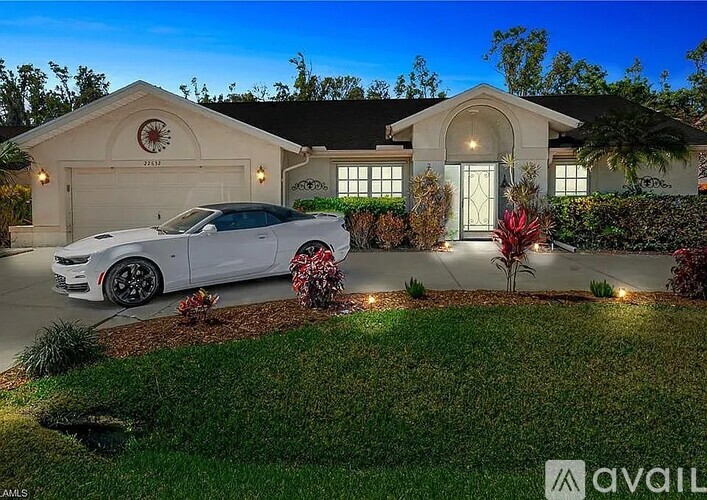 A white car is parked in front of a house with a garage.
