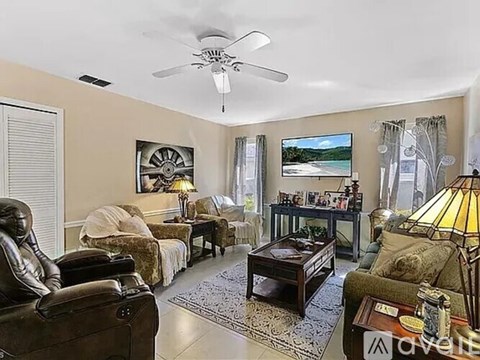A living room with a ceiling fan, a couch, a chair, a coffee table, and a painting on the wall.