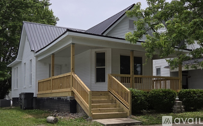 A white house with a black roof and a wooden deck.