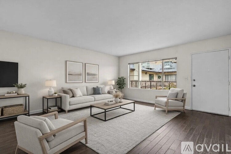A living room with a white couch, a grey armchair, a wooden coffee table, and a large window with a view of a building.