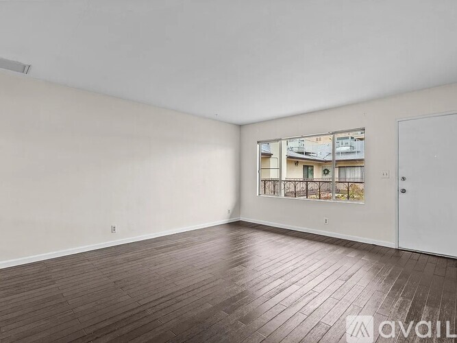 Empty room with wooden flooring and a window showing a view of other buildings.