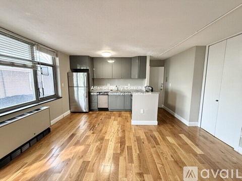 A spacious room with wooden flooring and a kitchen area with white cabinets and appliances.