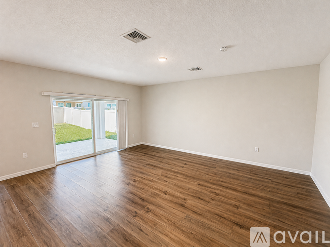 A spacious room with wooden flooring and a sliding glass door leading to a green outdoor area.
