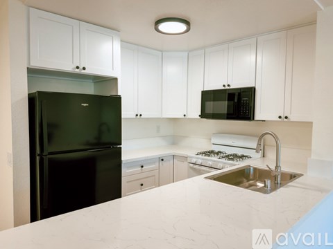 A kitchen with white cabinets and a black fridge.